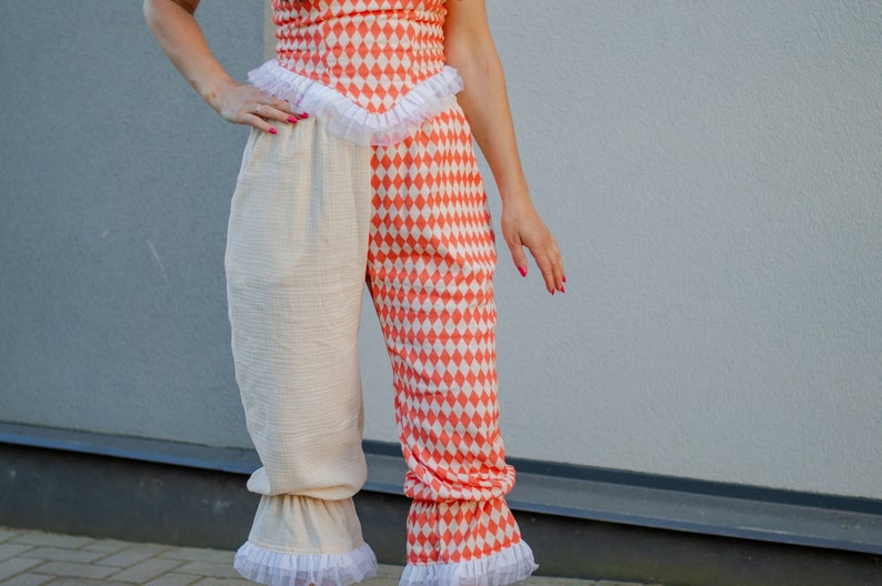 May include: A pair of pants with a white and orange diamond pattern. The pants have a ruffle trim at the bottom and are made of a soft, lightweight fabric.