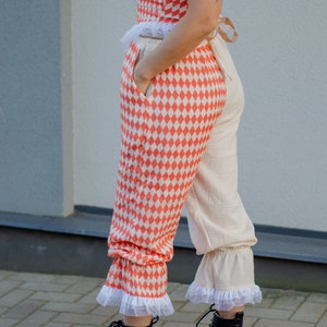 May include: A pair of pants with a checkered pattern in orange and white. The pants have a white ruffle at the bottom and are paired with black lace-up boots.