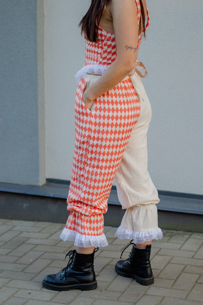 May include: A pair of pants with a checkered pattern in orange and white. The pants have a white ruffle at the bottom and are paired with black lace-up boots.