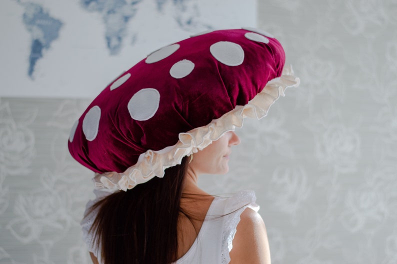 May include: A large, red velvet mushroom-shaped pillow with white polka dots and a white ruffled trim.