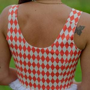 May include: A red and white checkered crop top with a white lace trim. The top has a scoop neck and a fitted bodice.