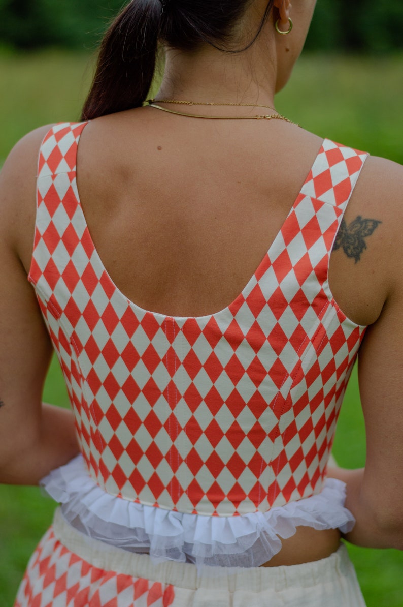 May include: A red and white checkered crop top with a white lace trim. The top has a scoop neck and a fitted bodice.