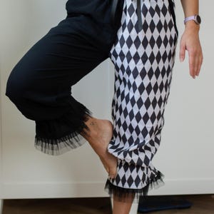 May include: Black and white harlequin-patterned pants with a contrasting black leg. The pants feature a ruffled hem and are part of a two-piece outfit. The top is a matching harlequin pattern with a lace-up front.