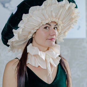 May include: A woman wearing a green velvet dress and a large white and green mushroom hat. The hat has a ruffled edge and is made of fabric.