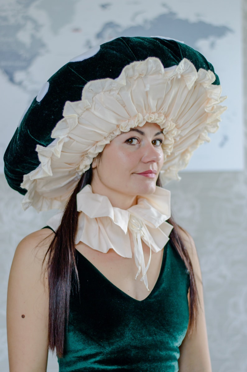 May include: A woman wearing a green velvet dress and a large white and green mushroom hat. The hat has a ruffled edge and is made of fabric.