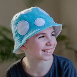 May include: A young person wearing a blue fleece bucket hat with white polka dots. The hat has a wide brim and is made of soft, fuzzy fabric.