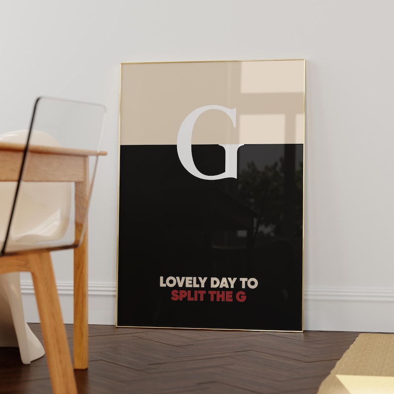 Pode incluir: Uma impress&atilde;o de arte emoldurada com uma borda dourada. A obra de arte &eacute; dividida horizontalmente, com uma se&ccedil;&atilde;o superior bege e uma se&ccedil;&atilde;o inferior preta. Uma grande letra branca "G" est&aacute; centralizada. O texto "LOVELY DAY TO SPLIT THE G" est&aacute; na parte inferior.