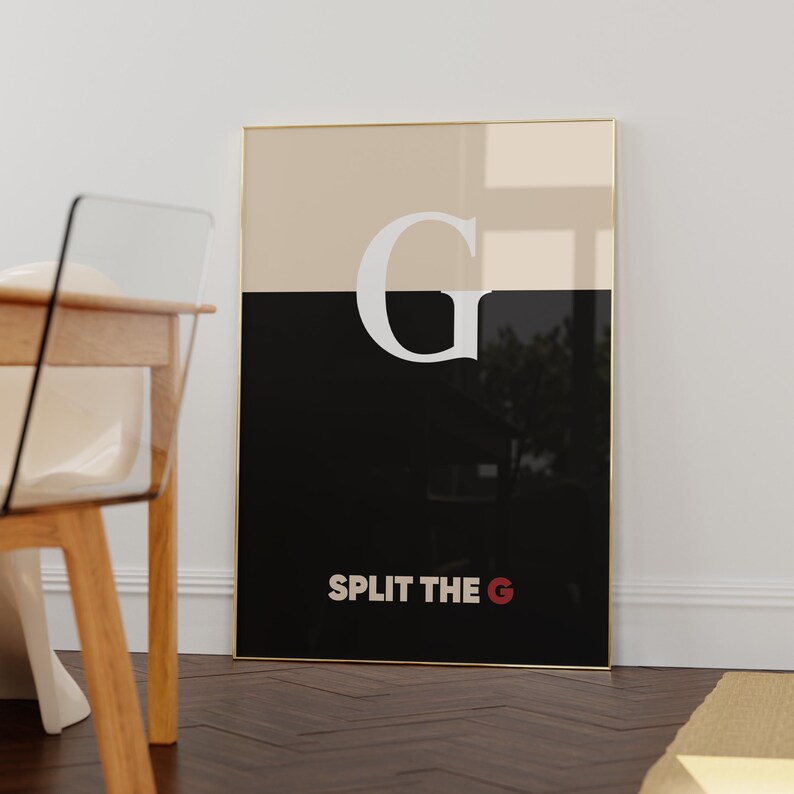 Pode incluir: Uma impress&atilde;o de arte emoldurada com uma moldura dourada. A obra de arte &eacute; dividida horizontalmente em duas se&ccedil;&otilde;es: uma metade superior bege e uma metade inferior preta. Uma grande letra branca "G" &eacute; centralizada, com o texto "SPLIT THE G" abaixo em branco e vermelho.