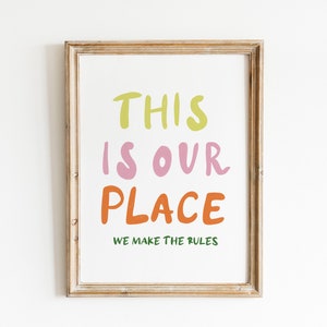 May include: A framed print with the text "This is our place. We make the rules." in colorful, handwritten font. The words "This" and "place" are in green and orange, "is" is in pink, and "our" is in light pink.
