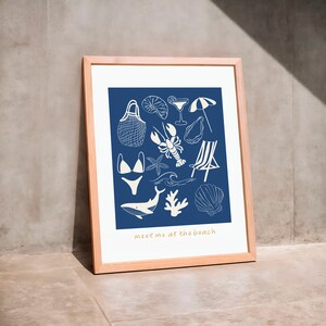 May include: A framed print with a blue background and white illustrations of beach-themed items, including a seashell, a lobster, a swimsuit, a beach chair, a wave, a starfish, a net bag, a cocktail glass, an umbrella, and a whale. The text "meet me at the beach" is at the bottom of the print.