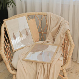 May include: Two framed prints featuring abstract floral designs in muted tones of brown and beige, displayed on a wicker chair with a beige throw blanket.