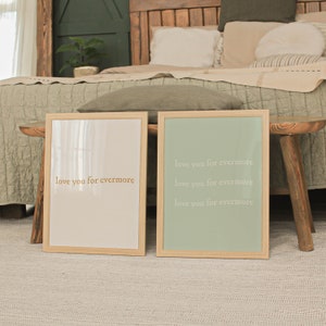 May include: Two framed prints with the text "love you for evermore" in a gold color. The print on the left has a white background and the print on the right has a light green background. The prints are sitting on a wooden table.