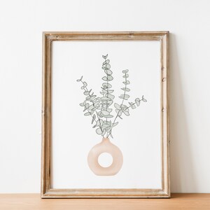 May include: A framed print of a line drawing of a vase with eucalyptus leaves in a light brown frame.