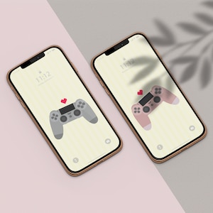 Puede incluir: Dos smartphones con marcos dorados muestran fondos de pantalla con un diseño de mando de videojuegos y un pequeño corazón rojo. El fondo es amarillo claro con rayas verticales. La hora es 11:12.