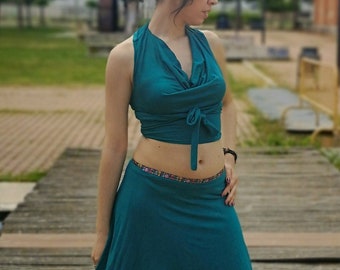 May include: A teal two-piece outfit consisting of a halter top and a handkerchief skirt. The top is tied at the waist, and the skirt has an asymmetrical hemline. The outfit is paired with black sandals with fringe.