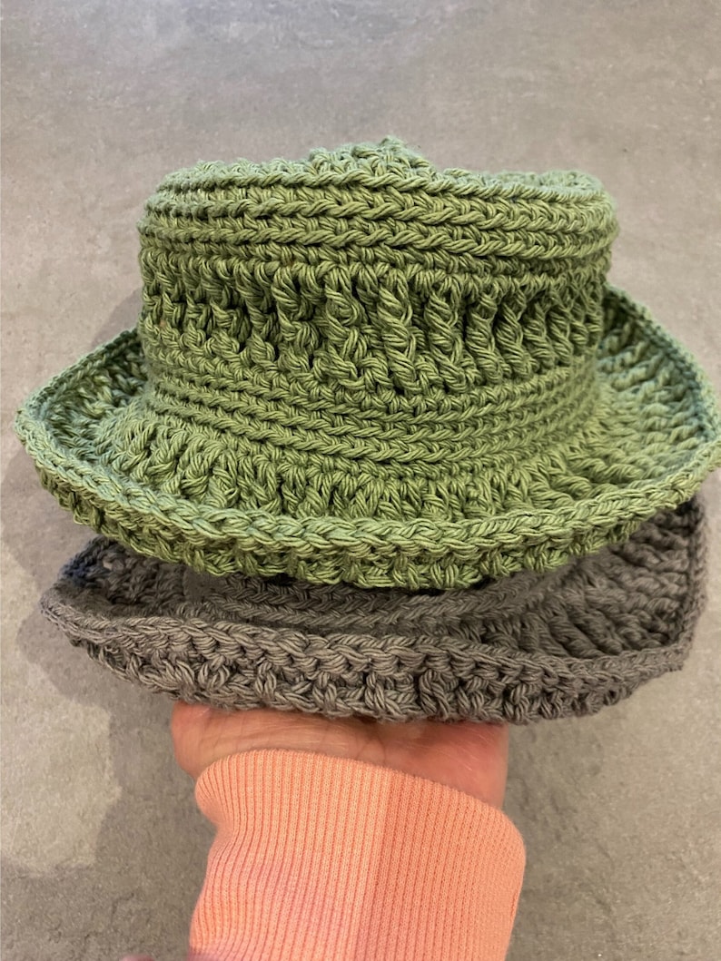 Op de afbeelding: Twee gebreide bucket-hoeden, een in groene kleur en een in grijze kleur, op elkaar gestapeld.