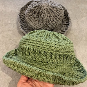 Op de afbeelding: Twee gebreide bucket-hoeden, een in lichtgroen en een in grijs.