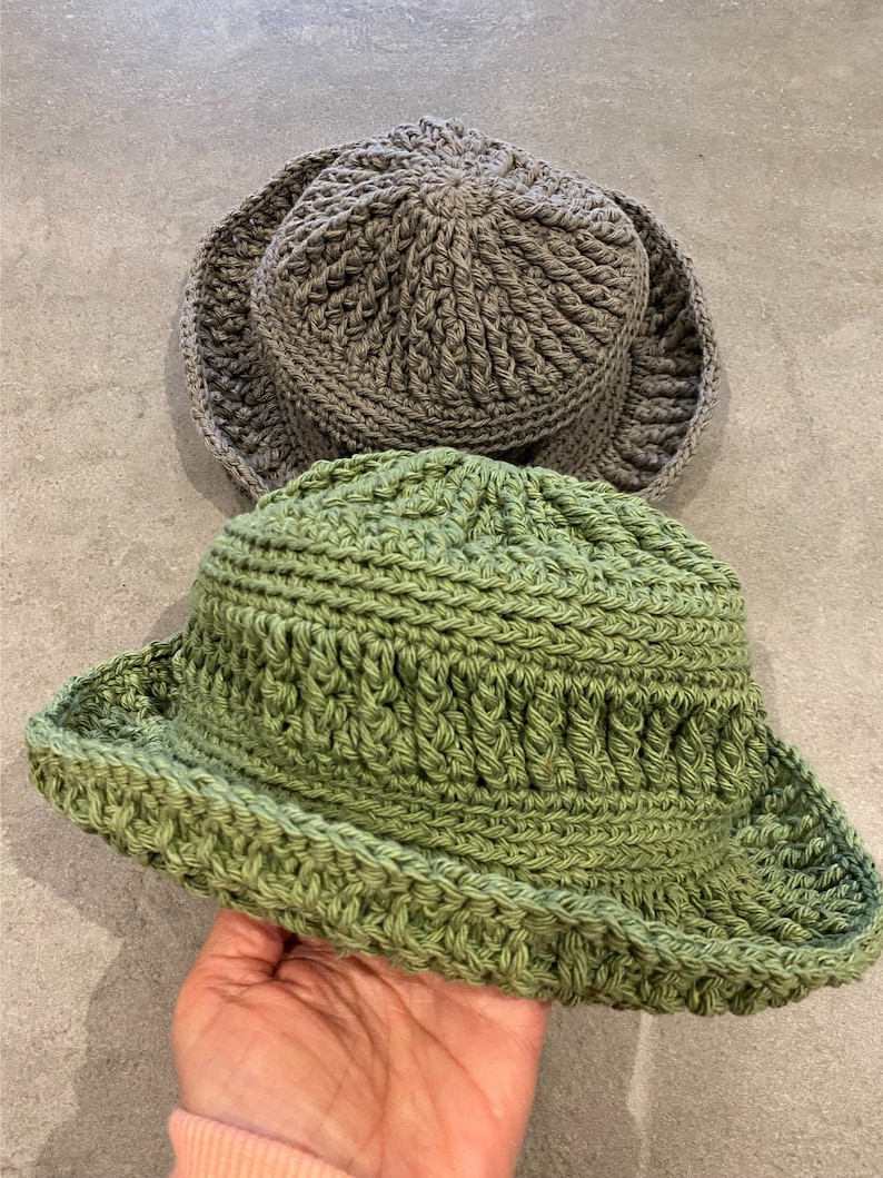 Op de afbeelding: Twee gebreide bucket-hoeden, een in lichtgroen en een in grijs.