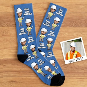 May include: Two blue socks with a repeating cartoon design of an engineer in a hard hat and safety vest. The text "ENGR. JUAN MARTINEZ" is printed on the socks. A photo is included.