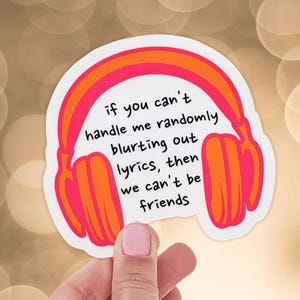 May include: A white sticker with a pink, orange, and red headphone design. The sticker has the text: "if you can't handle me randomly blurting out lyrics, then we can't be friends."