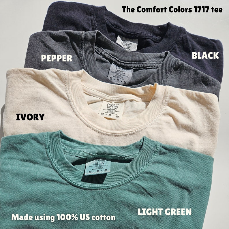 Puede incluir: Cuatro camisetas de diferentes colores: negro, pimienta, marfil y verde claro. Las camisetas est&aacute;n hechas de 100% algod&oacute;n estadounidense y tienen el texto "Comfort Colors 1717 tee" en la parte superior.
