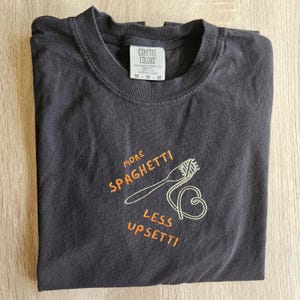 May include: Black t-shirt with white embroidery that says "More Spaghetti Less Upsetti" with a drawing of a fork and spaghetti.