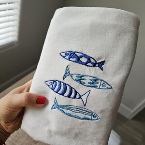 May include: White cotton dish towel with blue embroidered fish designs.