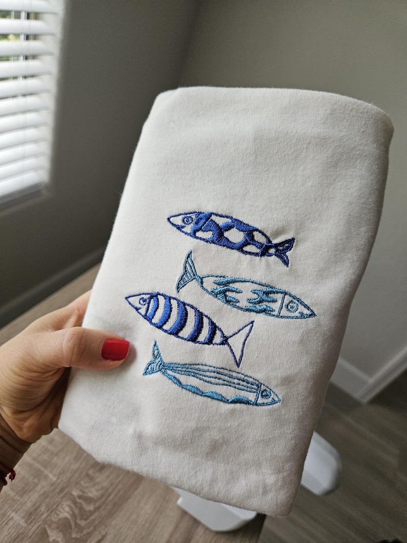 May include: White cotton dish towel with blue embroidered fish designs.