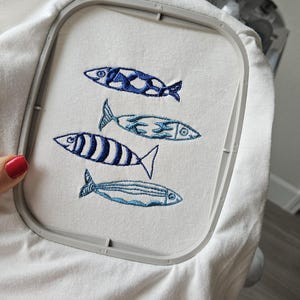 May include: White fabric with an embroidery hoop showing four blue and white fish designs.
