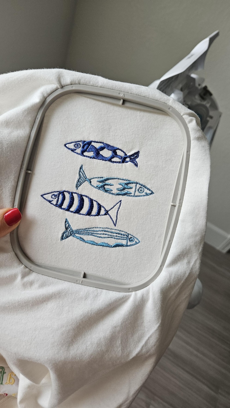 May include: White fabric with an embroidery hoop showing four blue and white fish designs.