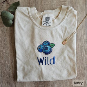 May include: Ivory t-shirt with embroidered blueberries and the word "Wild".