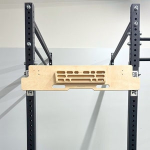 May include: A black metal pull-up bar with a wooden climbing hold attached to the top. The bar is mounted to a black metal frame with multiple holes.