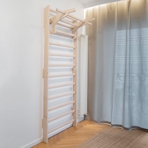 Può includere: Un telaio da arrampicata in legno montato a parete con una scala e sbarre per trazioni. Il telaio è realizzato in legno di colore chiaro ed è installato contro un muro bianco. Il telaio è progettato per l'esercizio fisico e il fitness.