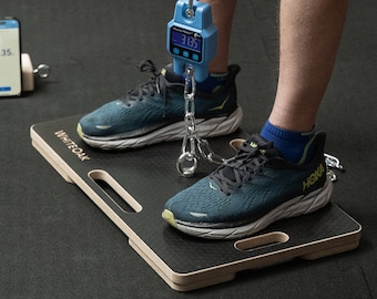 May include: A person standing on a wooden platform with a digital scale attached to their foot. The scale reads "3.85". The person is wearing blue and black running shoes.