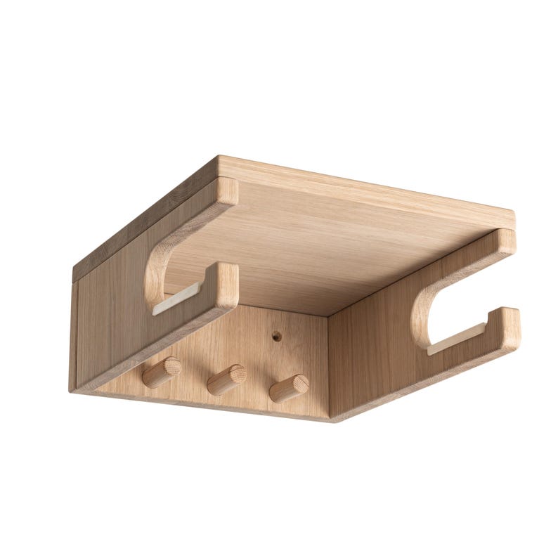 May include: A light-colored wooden wall-mounted shelf with a rectangular top and two curved cutouts on the sides. Three small wooden pegs are positioned below the shelf. The shelf is made of light-colored wood.