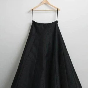 May include: A black maxi skirt hanging on a wooden hanger. The skirt is made of a smooth, flowing fabric and has a simple, elegant design.