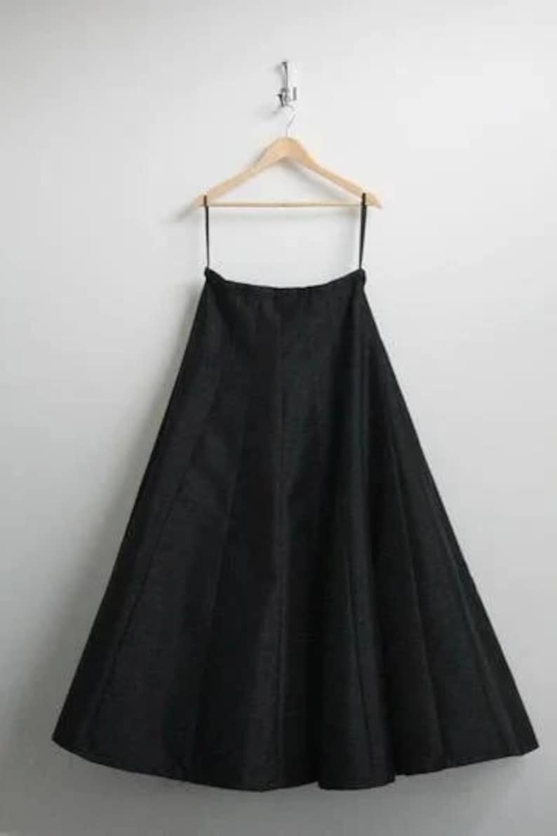 May include: A black maxi skirt hanging on a wooden hanger. The skirt is made of a smooth, flowing fabric and has a simple, elegant design.