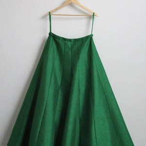 May include: A green, full-length skirt with pleats hanging on a wooden hanger.