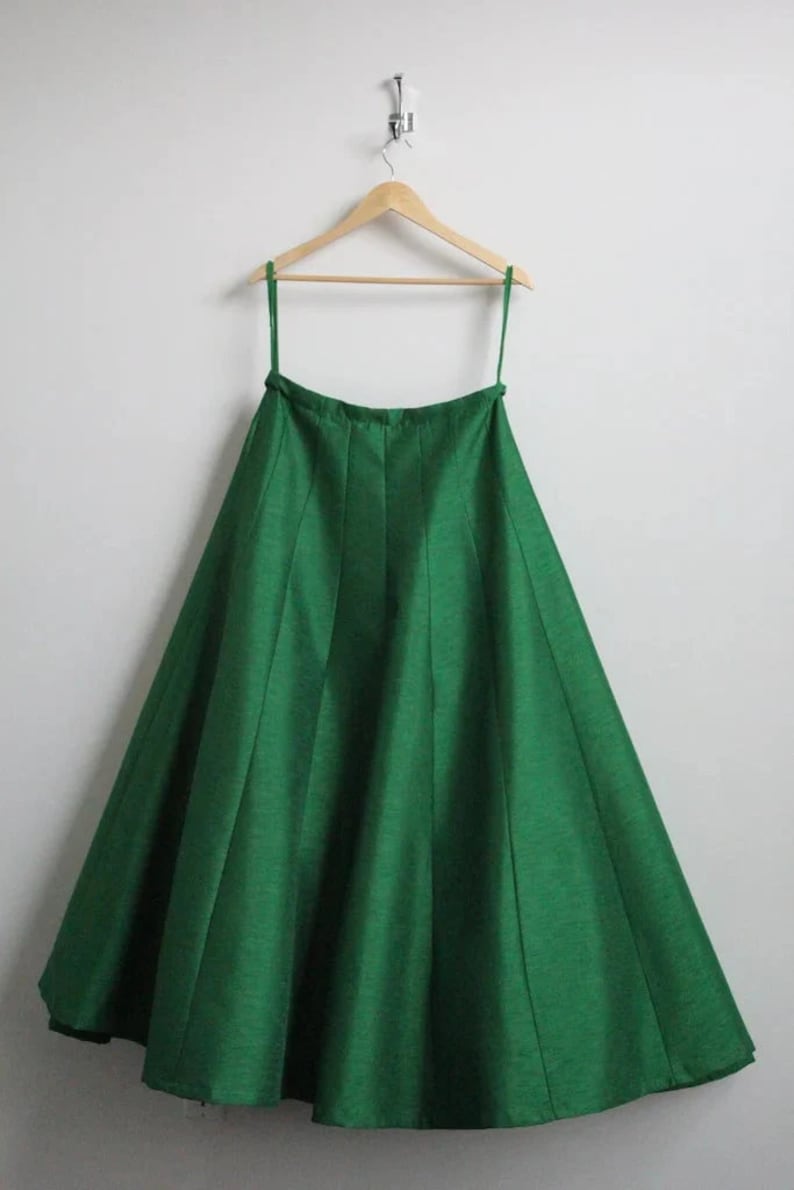 May include: A green, full-length skirt with pleats hanging on a wooden hanger.