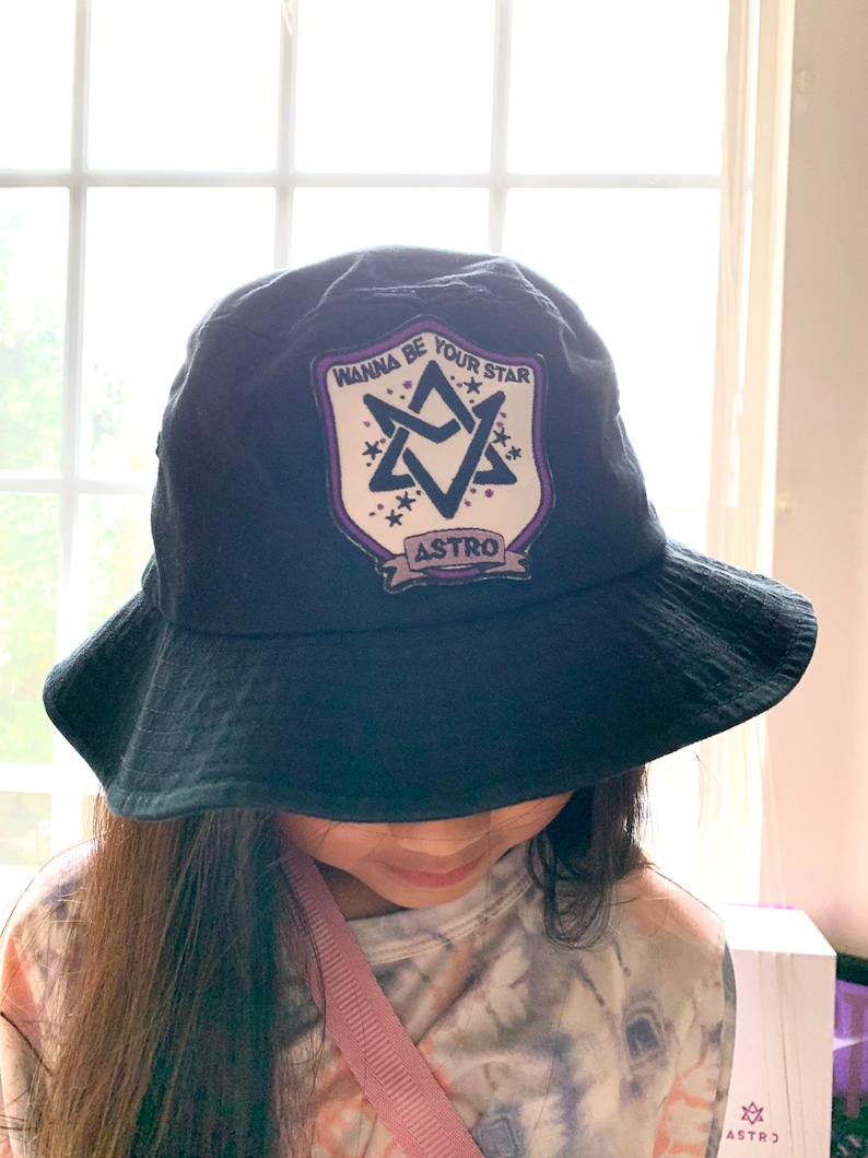 May include: Black bucket hat with a white patch featuring a purple star with the text "Wanna Be Your Star" and "ASTRO" underneath.