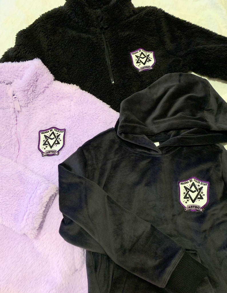 May include: Three different styles of sweatshirts with a purple and white patch that says "Wanna Be Your Star" and "ASTRO" in black lettering. The sweatshirts are black, purple, and black with a hood.
