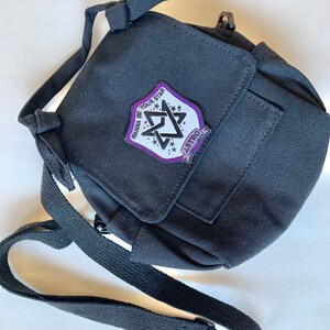 May include: Black canvas crossbody bag with a purple and white patch that says "Wanna Be Your Star" and "ASTRO" in a star shape.