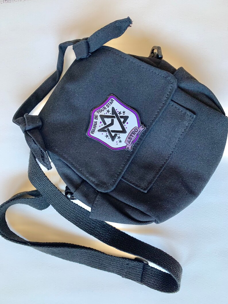 May include: Black canvas crossbody bag with a purple and white patch that says "Wanna Be Your Star" and "ASTRO" in a star shape.