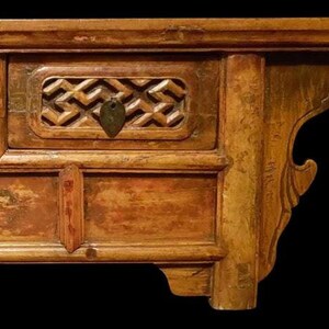 May include: A vintage wooden table with two drawers and intricate carvings. The table has a dark brown finish with a distressed look. The drawers have brass handles and are decorated with a geometric pattern.
