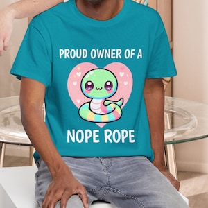 May include: Two short-sleeved t-shirts, one charcoal gray and one teal, each featuring a cartoon snake design inside a pink heart. The text "PROUD OWNER OF A NOPE ROPE" is printed above and below the snake illustration.