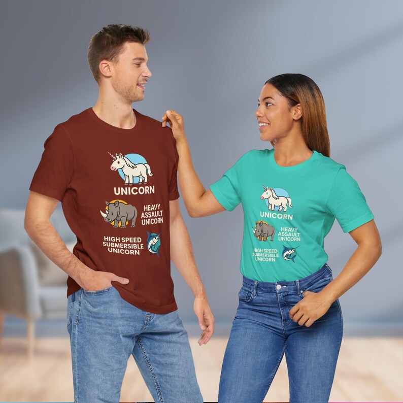May include: Two people wearing matching t-shirts. The shirts are a maroon and teal color. Each shirt has a graphic of a unicorn, a rhino, and a shark with the words "UNICORN", "HEAVY ASSAULT UNICORN", and "HIGH SPEED SUBMERSIBLE UNICORN".