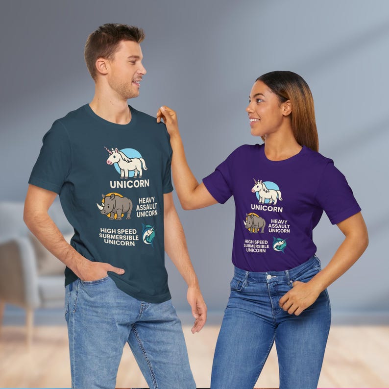 May include: Two people wearing matching graphic t-shirts. The shirts are teal and purple, each featuring a unicorn design with the text "UNICORN", "HEAVY ASSAULT UNICORN", and "HIGH SPEED SUBMERSIBLE UNICORN". The shirts are paired with blue jeans.