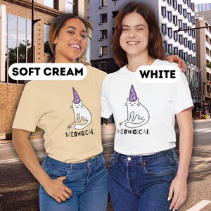 Pu&ograve; includere: T-shirt color crema e bianche con un fantasioso disegno di gatto con cappello da mago e la scritta "MEOWGICAL". Il gatto &egrave; nero e bianco, con un cappello viola. Le magliette sono abbinate a jeans blu.