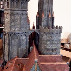 May include: A detailed model of a medieval castle with multiple towers, arched windows, and red tile roofs. The castle is constructed from gray stone with copper accents, showcasing a miniature architectural design.