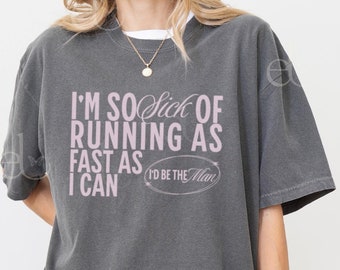 May include: A dark gray t-shirt with a pink graphic that reads "I'm so sick of running as fast as I can I'd be the man".